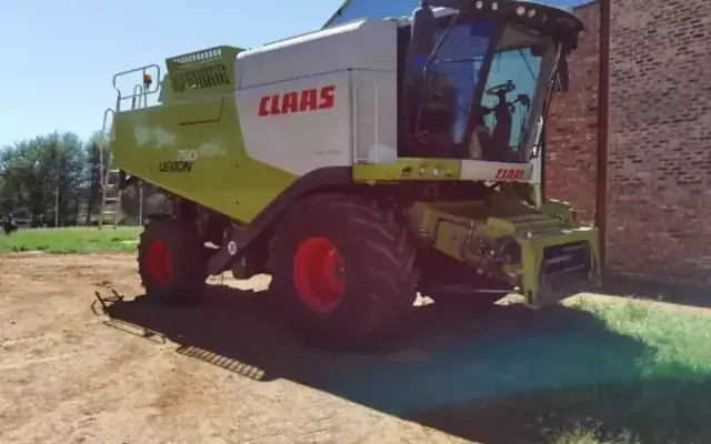 A Claas Lexion 750 combine harvester standing on a dirt yard next to a brick shed